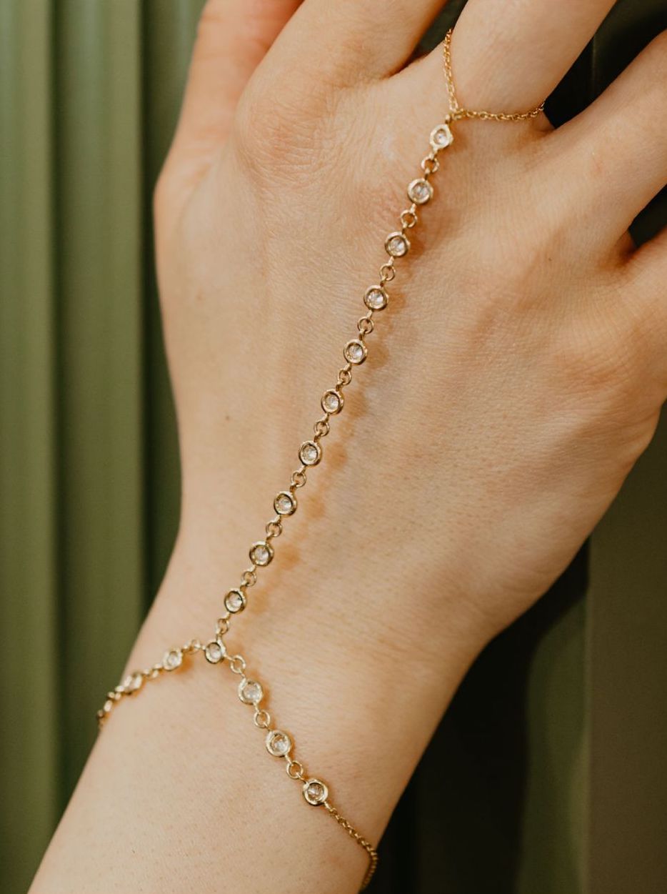 Multi Bezel Hand Chain is made in 18kt yellow gold, a ring attached to a bracelet with diamond bezels. 